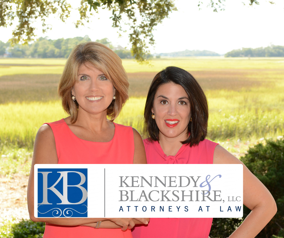 Two attorneys standing outdoors above the Kennedy & Blackshire Attorneys at Law logo with a coastal marsh background.